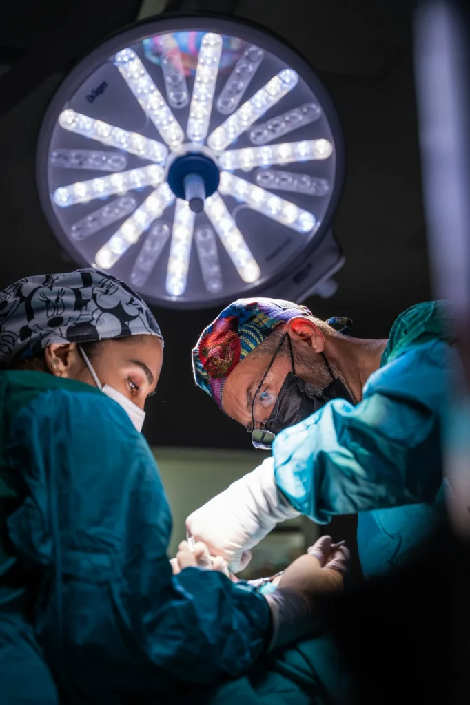 Two surgeons performing a medical procedure under bright surgical lights, representing healthcare risk management and regulatory oversight.