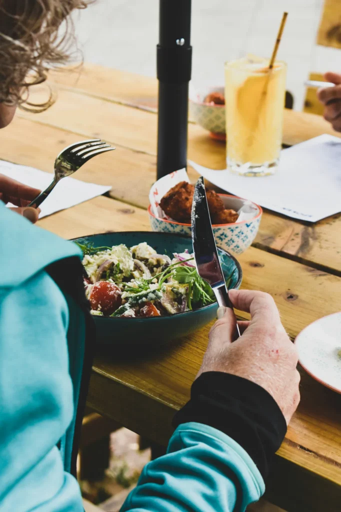 Close up of people dining at a restaurant table with a fresh salad bowl, representing the food and beverage sector and regulatory needs for hospitality businesses.