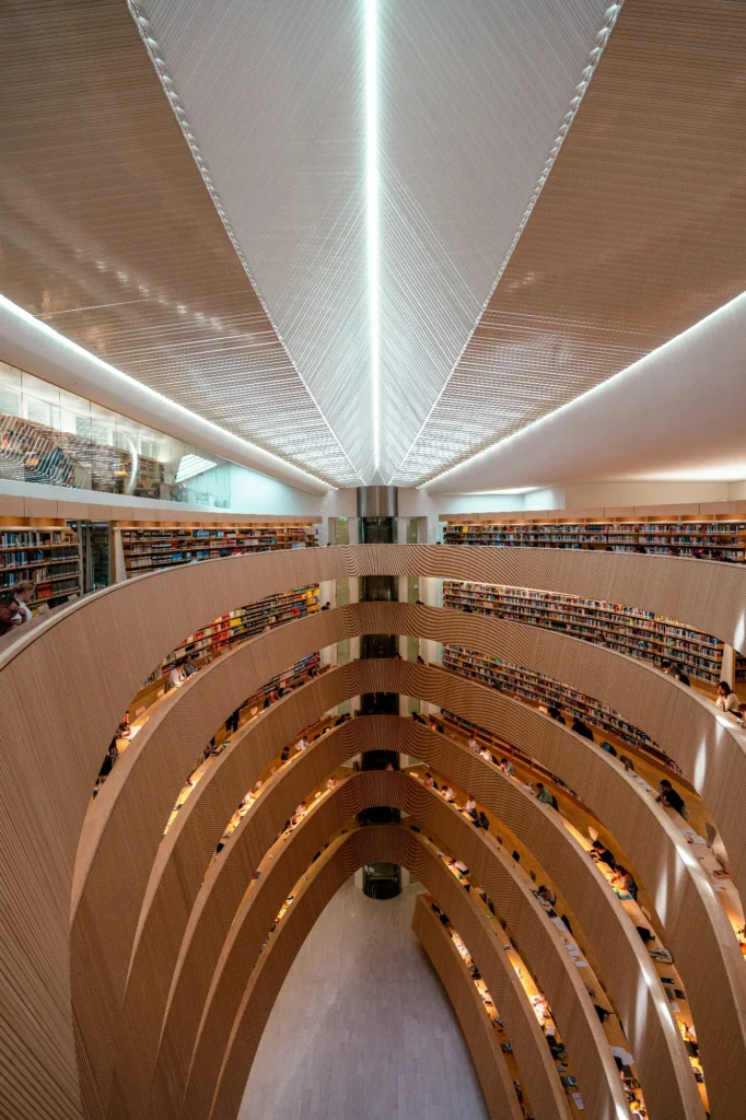 Interior of a modern multi level library with curved shelves and study areas, symbolizing educational infrastructure and learning environments.