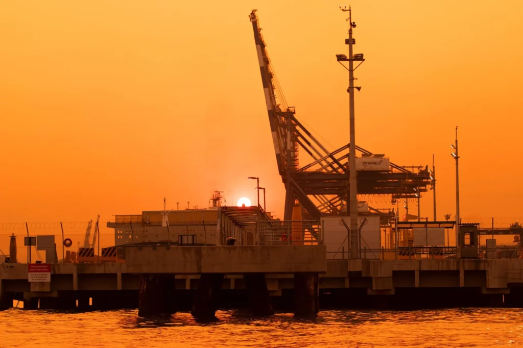 Port crane and shipping terminal at sunset showcasing operational risk management and logistics law services offered by THINC Dubai.