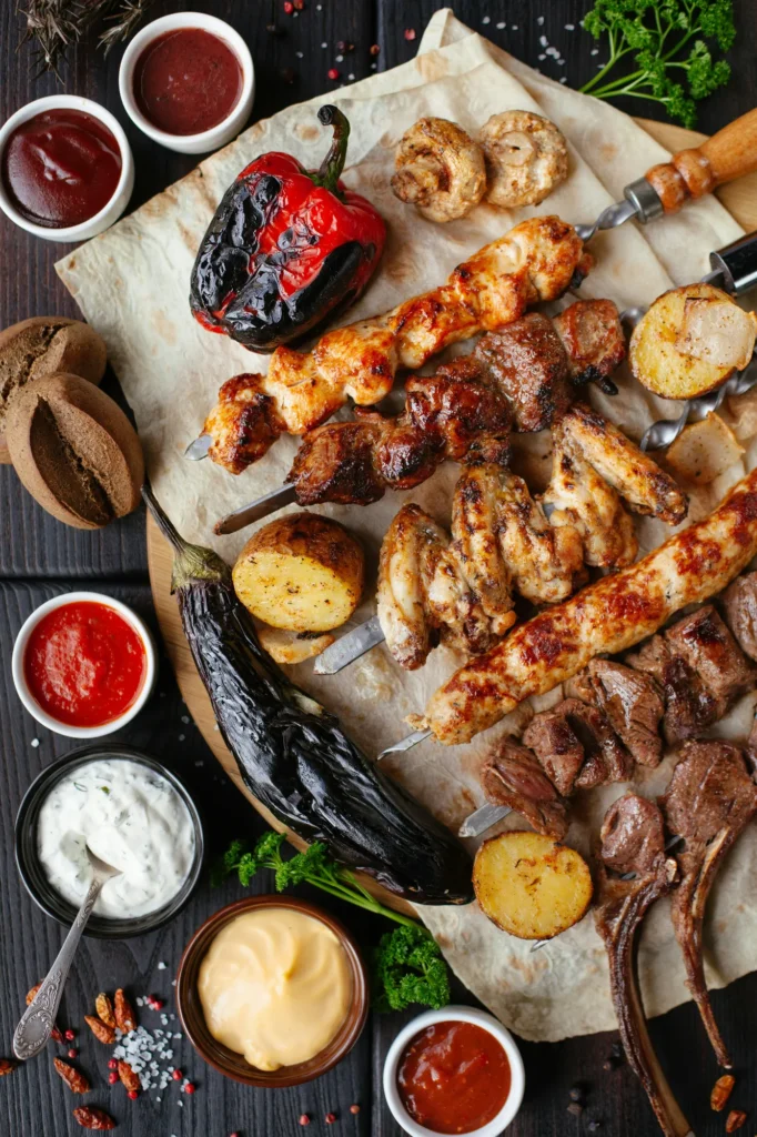 Assortment of grilled meats, kebabs, vegetables, and sauces displayed on a table, symbolizing food safety, labelling, halal certification, and compliance in the food and beverage industry.
